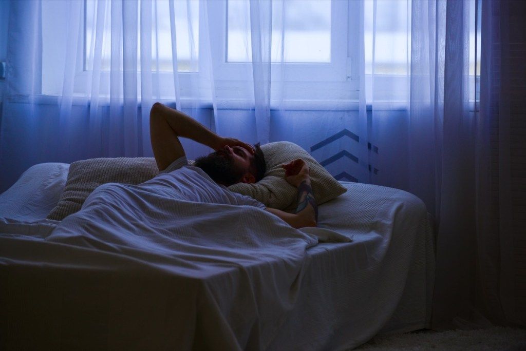 ผู้ชายนอนอยู่บนเตียงโดยสวมเสื้อเชิ้ต