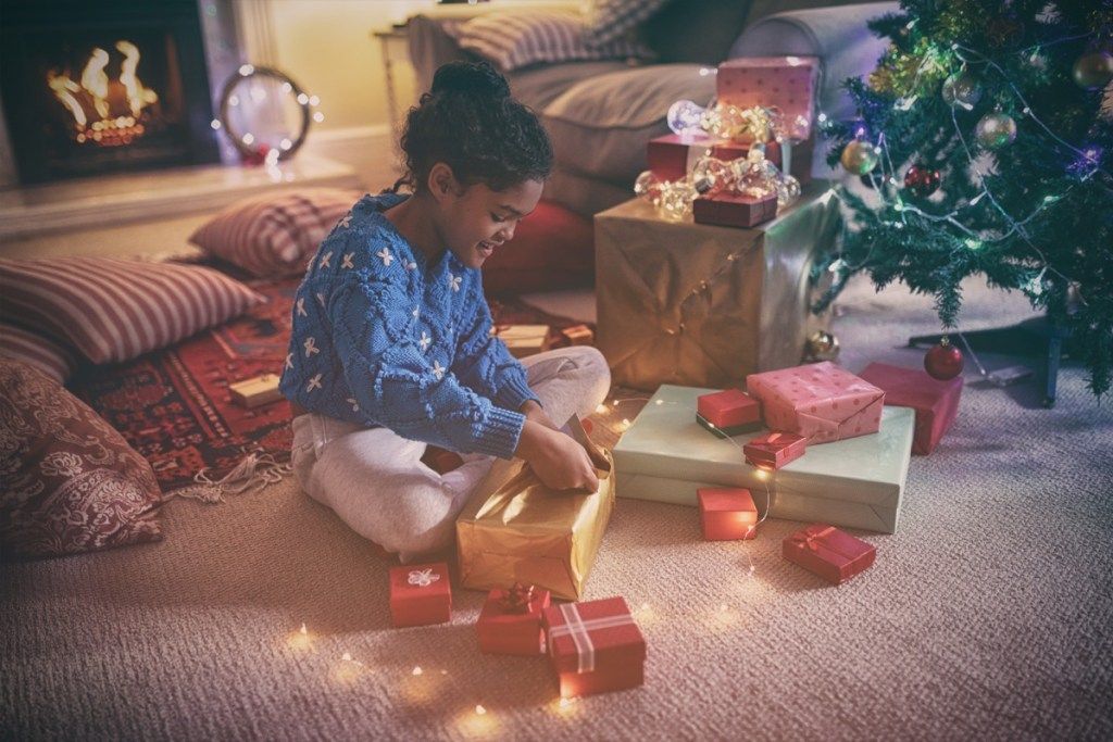 fetiță desfăcând cadouri în fața șemineului în dimineața de Crăciun