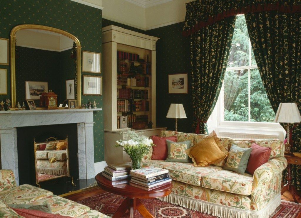 Cermin emas di atas perapian marmer di ruang tamu tahun sembilan puluhan, wallpaper hijau, tirai bermotif, sofa bunga