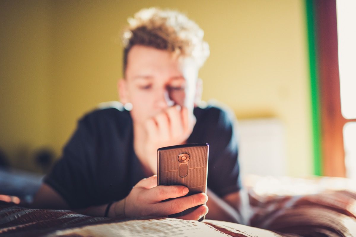 Dospievajúci chlapec používa svoj chytrý telefón ležiac ​​na posteli