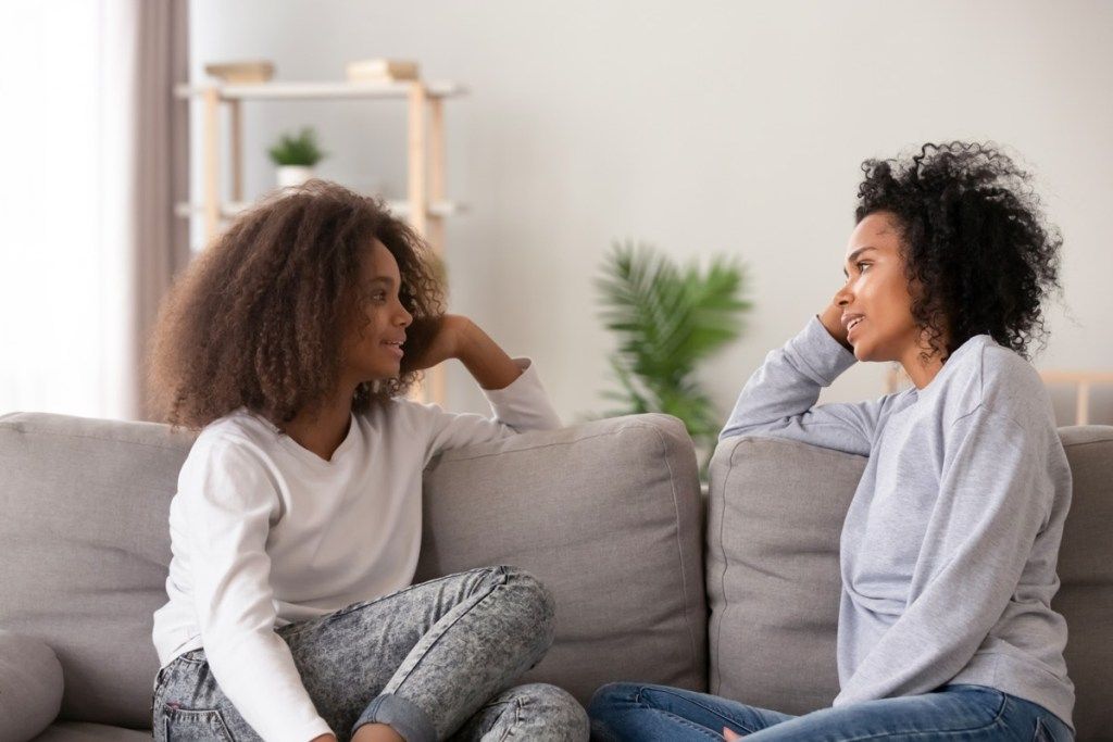mãe negra e filha conversando no sofá