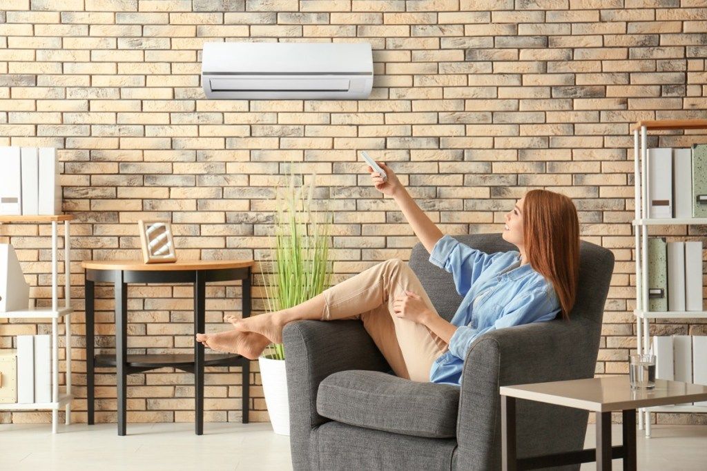 nainen säätää ilmastointilaitetta, huonot kodin kunnostustyöt