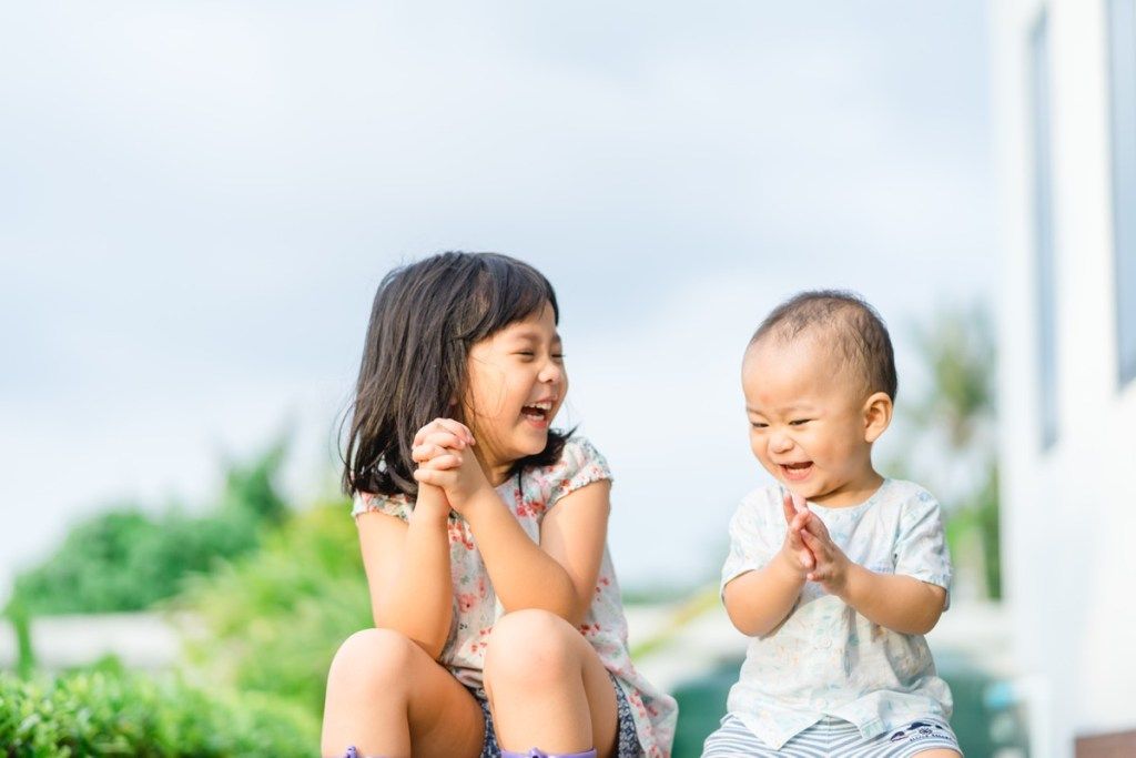 भाई-बहन हँसते हैं और एक साथ खेलते हैं, बीच का बच्चा