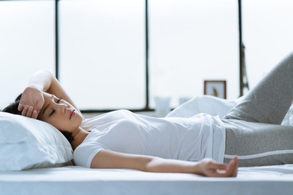 ženska, ki leži bolna v postelji z resnimi simptomi prehlada, glavobolom in vročino