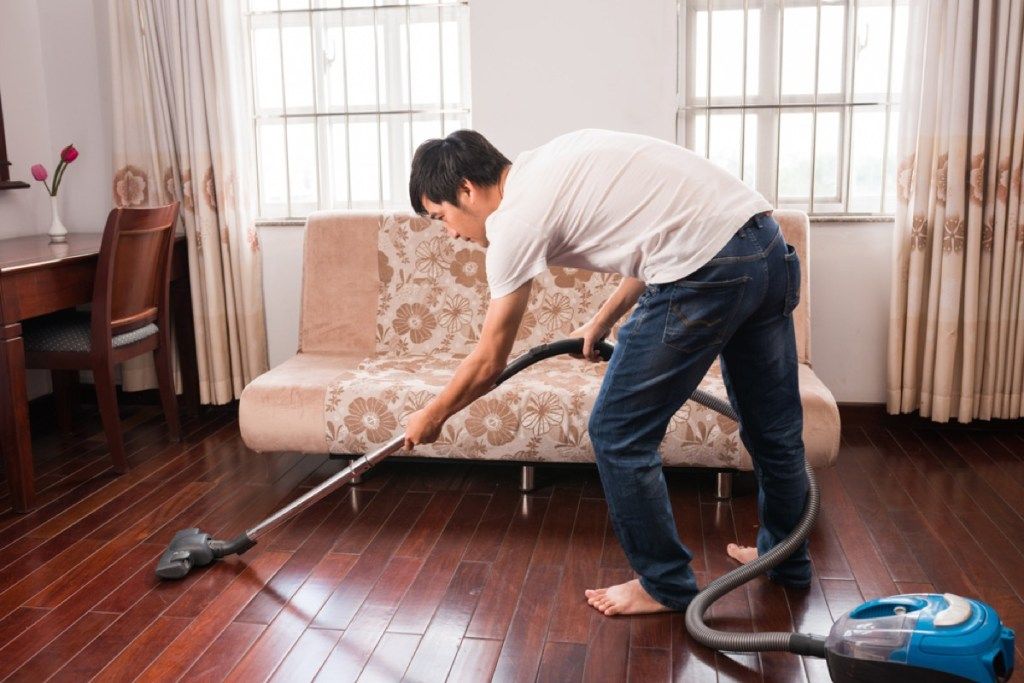 男は床を掃除機で掃除し、ヒントを掃除機で掃除する