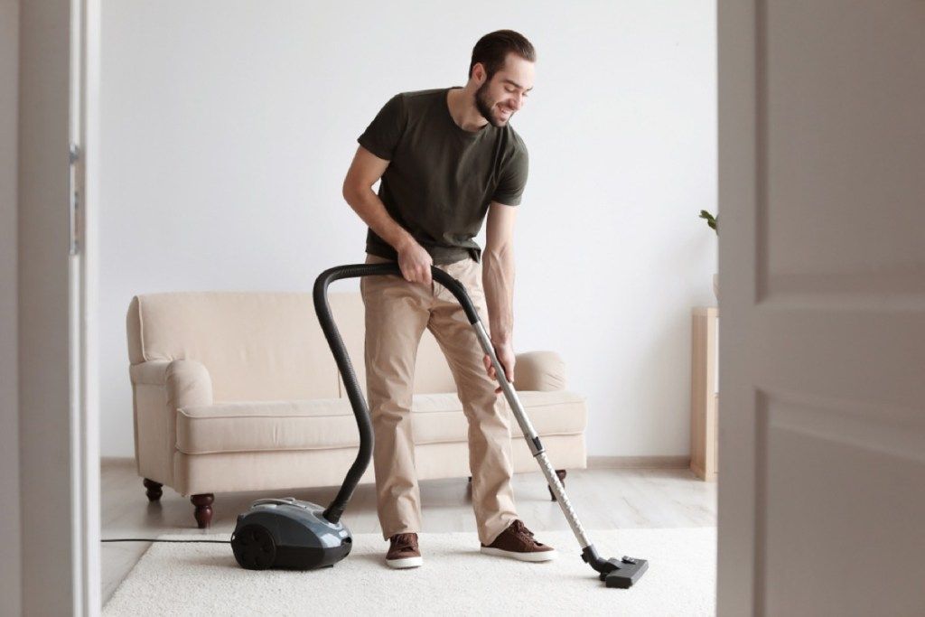男はカーペットを掃除機で掃除し、アタッチメントの高さを調整し、ヒントを掃除機で掃除します