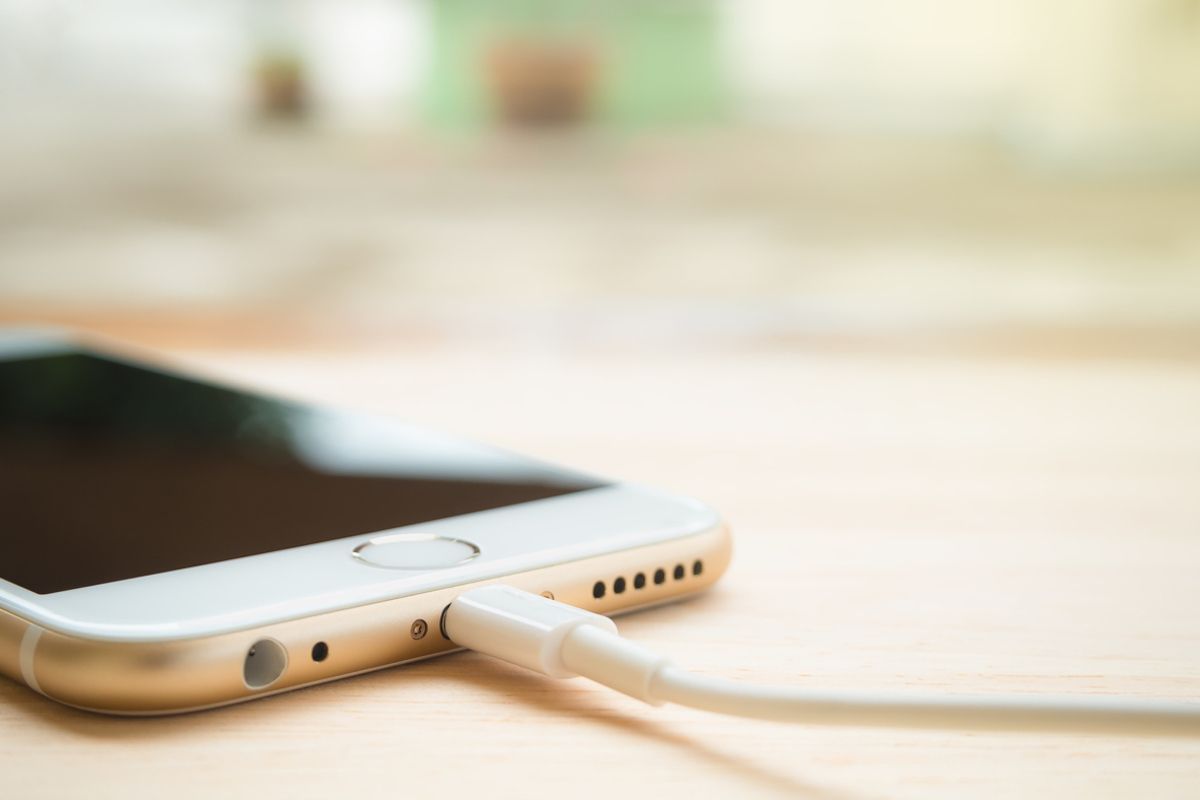 Slika izbliza Apple iPhone 6S koji se puni Lightning USB kabelom na drvenom stolu
