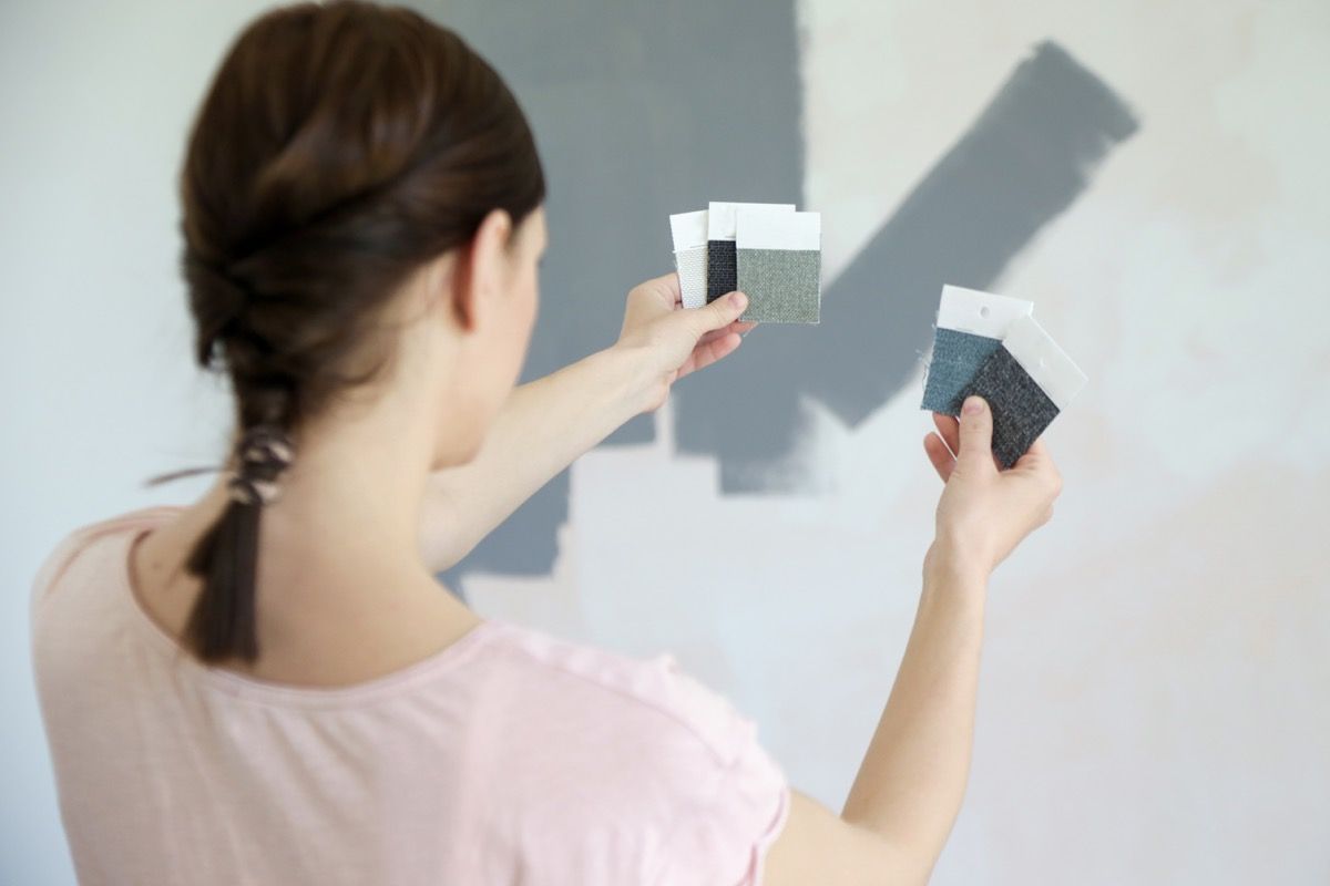 نوجوان عورت اپنی دیوار کے لئے بھوری رنگ کے پینٹ سویچوں کے درمیان انتخاب کرتی ہے