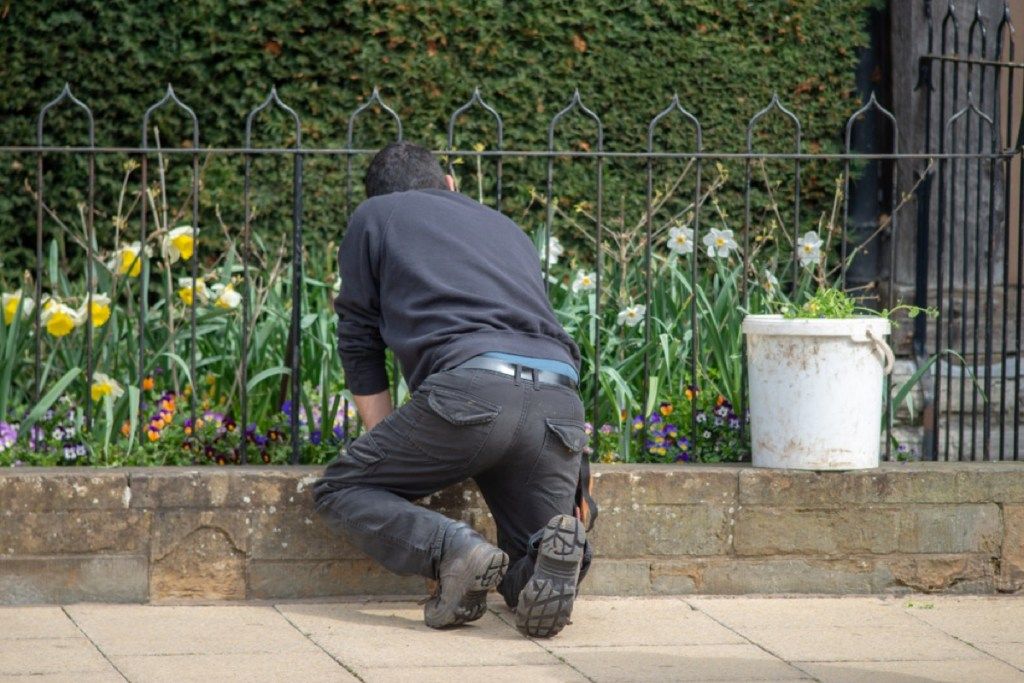 mladenič v črnih hlačah in črni srajci, ki sadi skozi ograjo na urbani ulici