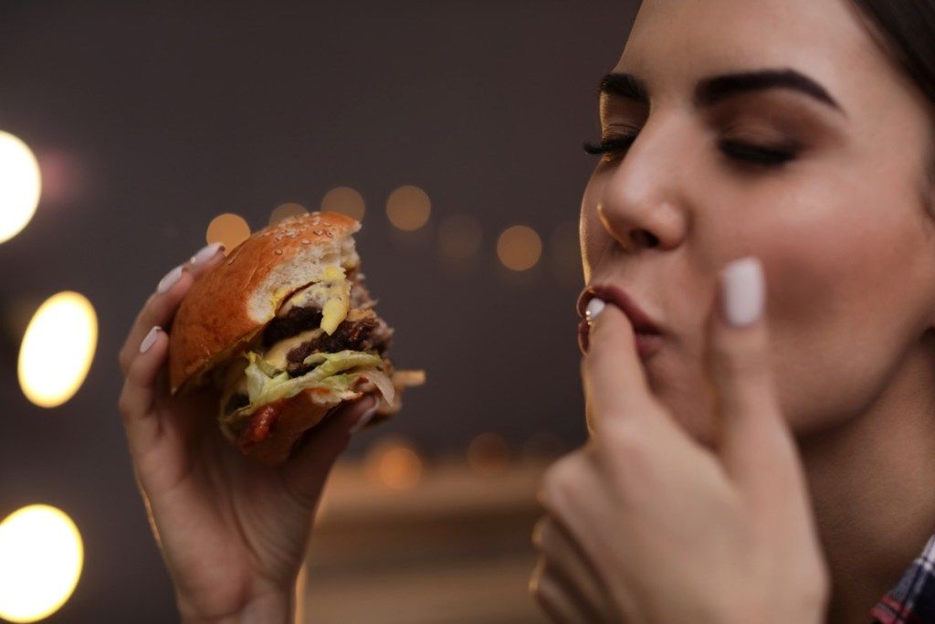 Sieviete, laizīdama pirkstus, baudot Burger BBQ etiķetes kļūdas
