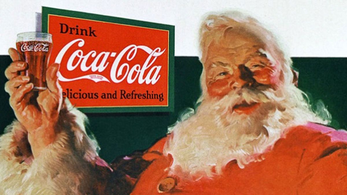 Božiček drži kozarec sode coca cole, v ozadju pa reklamo za pijačo coca cola