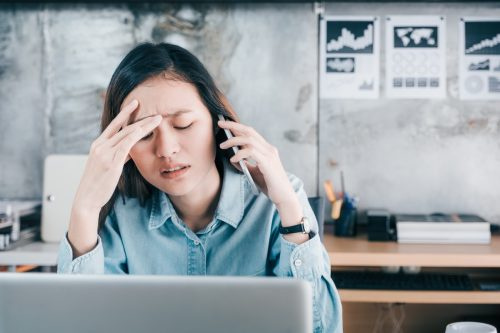   Стресирана креативна дизайнерка покрива лицето си с ръка и се чувства разстроена, докато говори по мобилен телефон с клиент пред лаптоп компютър