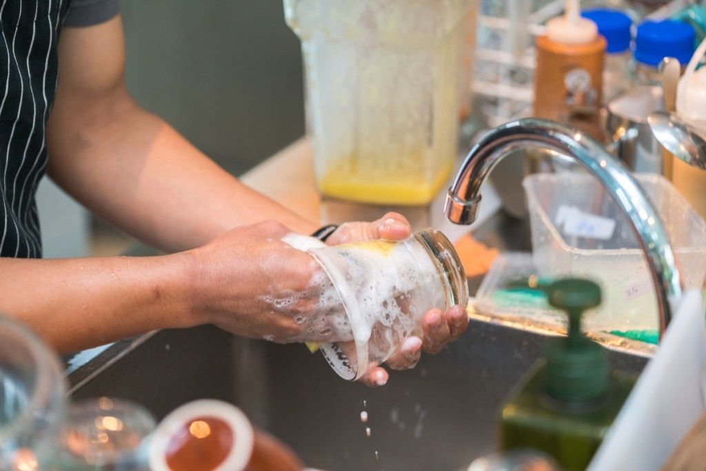 ผู้ชายกำลังทำความสะอาดถ้วยแก้วในอ่างล้างจาน