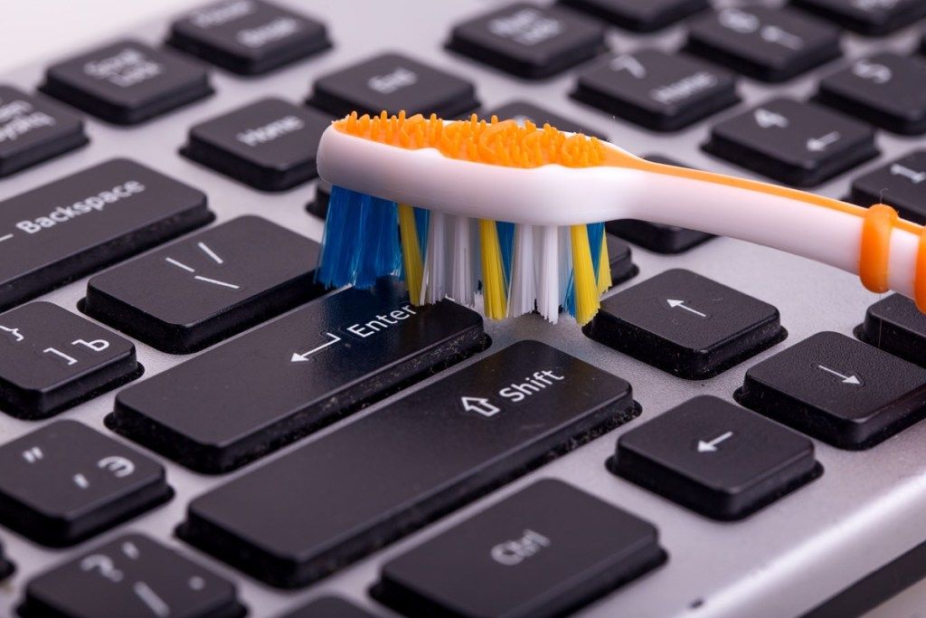 एक टूथब्रश क्लीनिंग Hacks के साथ एक कीबोर्ड की सफाई करने वाला व्यक्ति