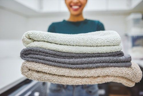 Artimas kadras - moteris, namuose laikanti šūsnį rankšluosčių