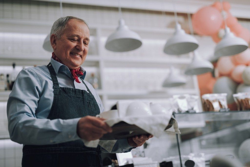 Taille portrait de travailleur de café masculin regardant une boisson chaude et souriant. Il porte un élégant foulard rouge