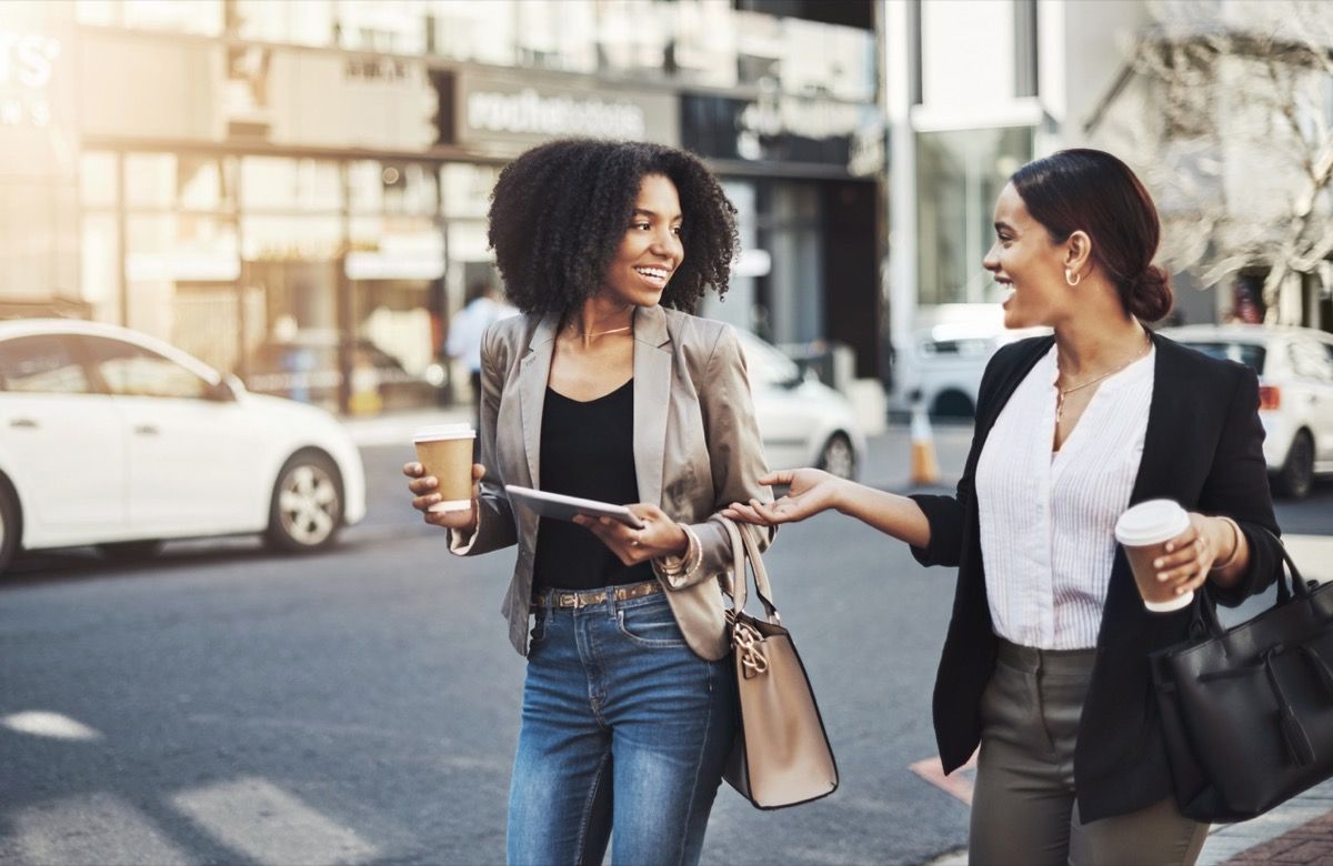 svart forretningskvinne og latina forretningskvinne som chatter med kaffe på gaten