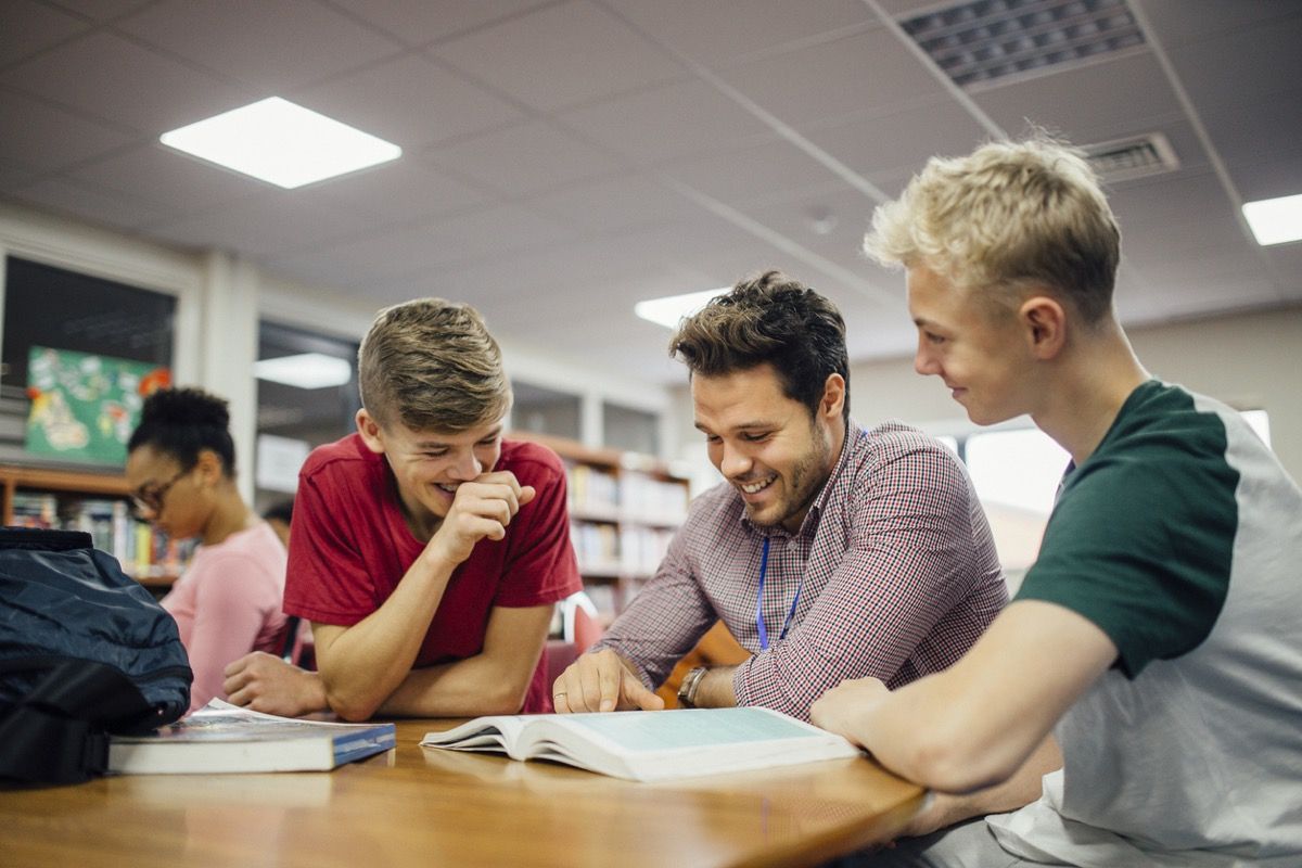 бял мъжки учител, който се смее с младите си ученици, докато гледа книга