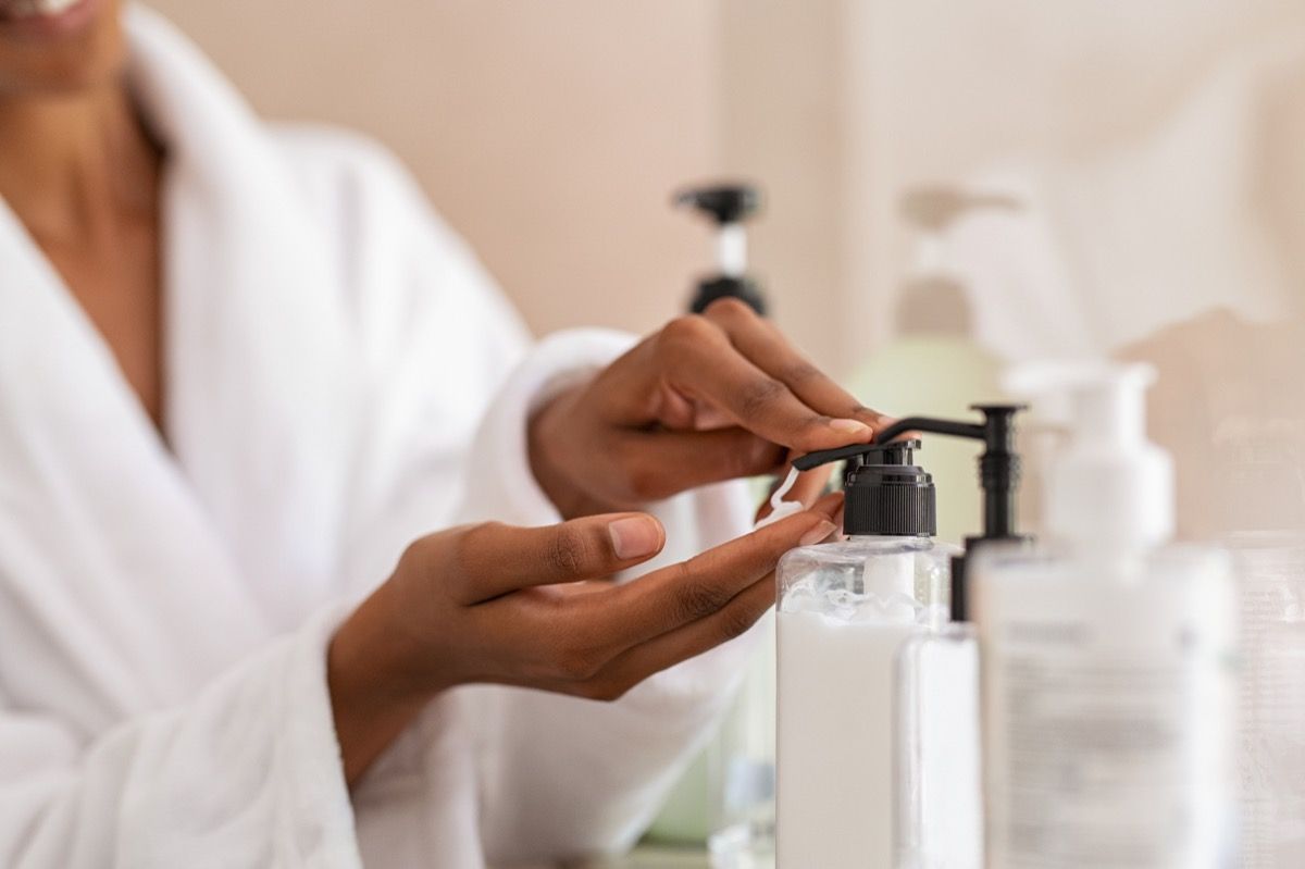 tay phụ nữ sử dụng xà phòng nước mỹ phẩm trong phòng tắm. Cận cảnh bàn tay trong áo choàng tắm bằng dụng cụ phân phối kem dưỡng thể sau khi tắm