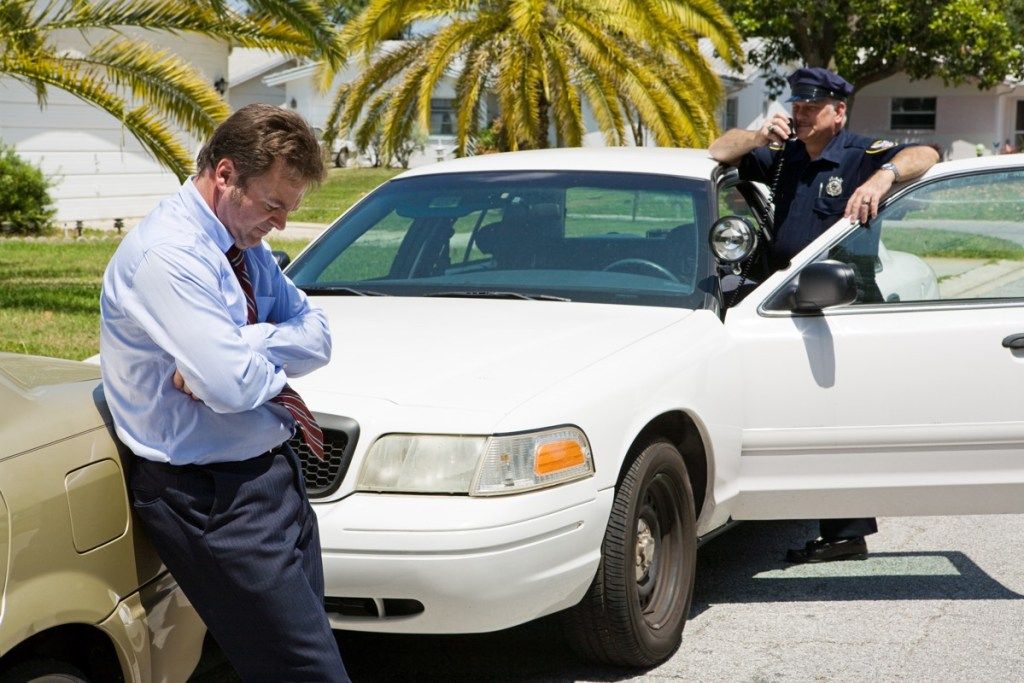 мъж, спрян от полицията, стоящ пред тайните на полицейския автомобил