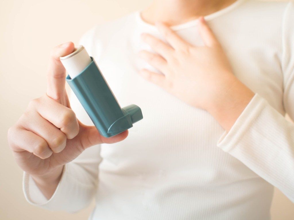 Wanita yang memegang inhaler asma, mengasuh lebih sulit