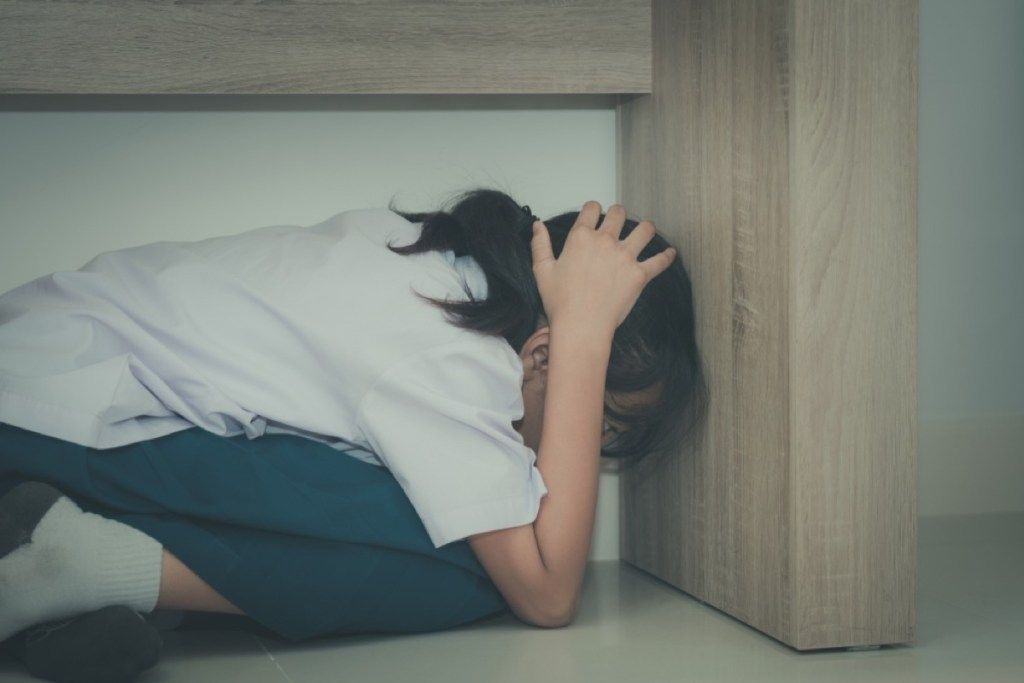 युवा लड़की डेस्क के नीचे छिपती है, पालन-पोषण कठिन है