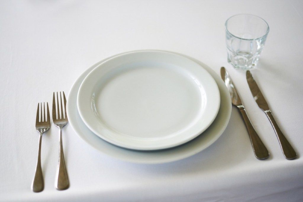 pratos brancos e dois conjuntos de garfos e facas na toalha de mesa branca