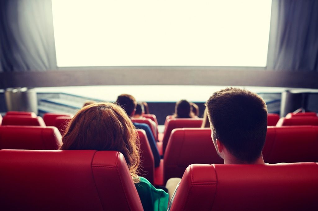 คู่รักนั่งอยู่ที่โรงภาพยนตร์ในที่นั่งสีแดงมองไปที่หน้าจอ