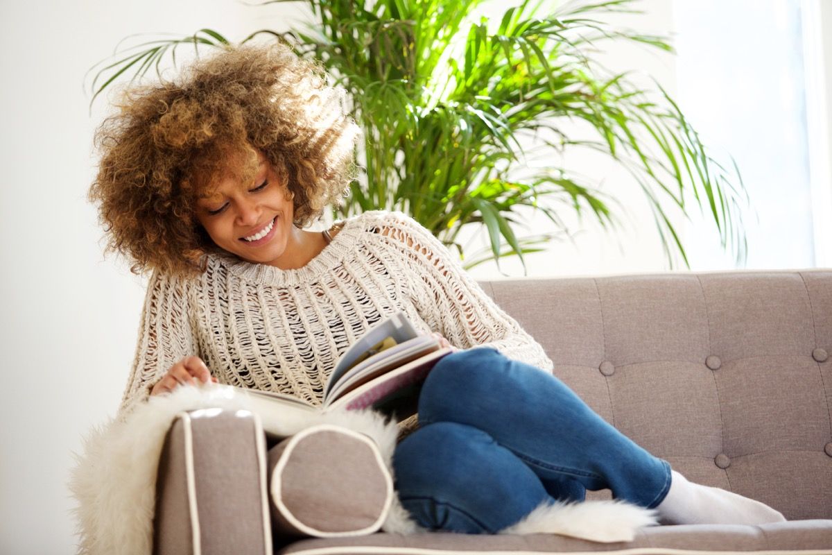 Retrato, de, atractivo, mujer americana africana, sentado, en, sofá, libro de lectura