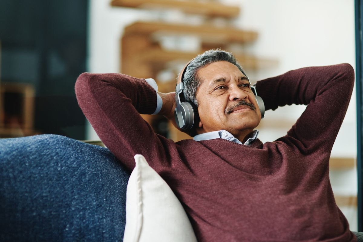 Senior hombre de color escuchando música en el sofá con las manos detrás de la cabeza