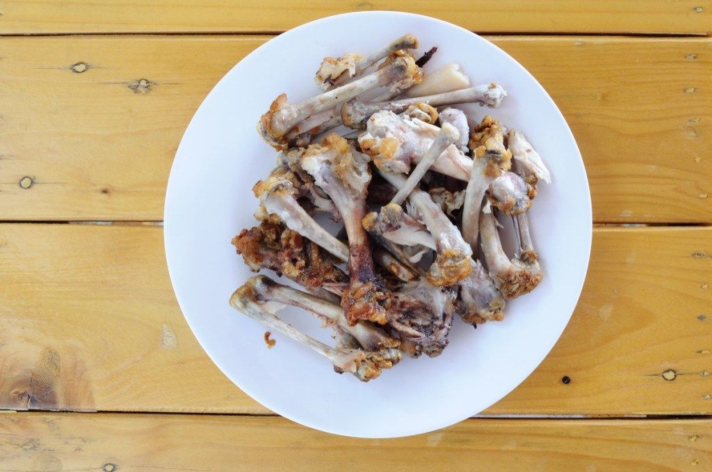 бяла чиния на дървена маса с пилешки кости върху нея