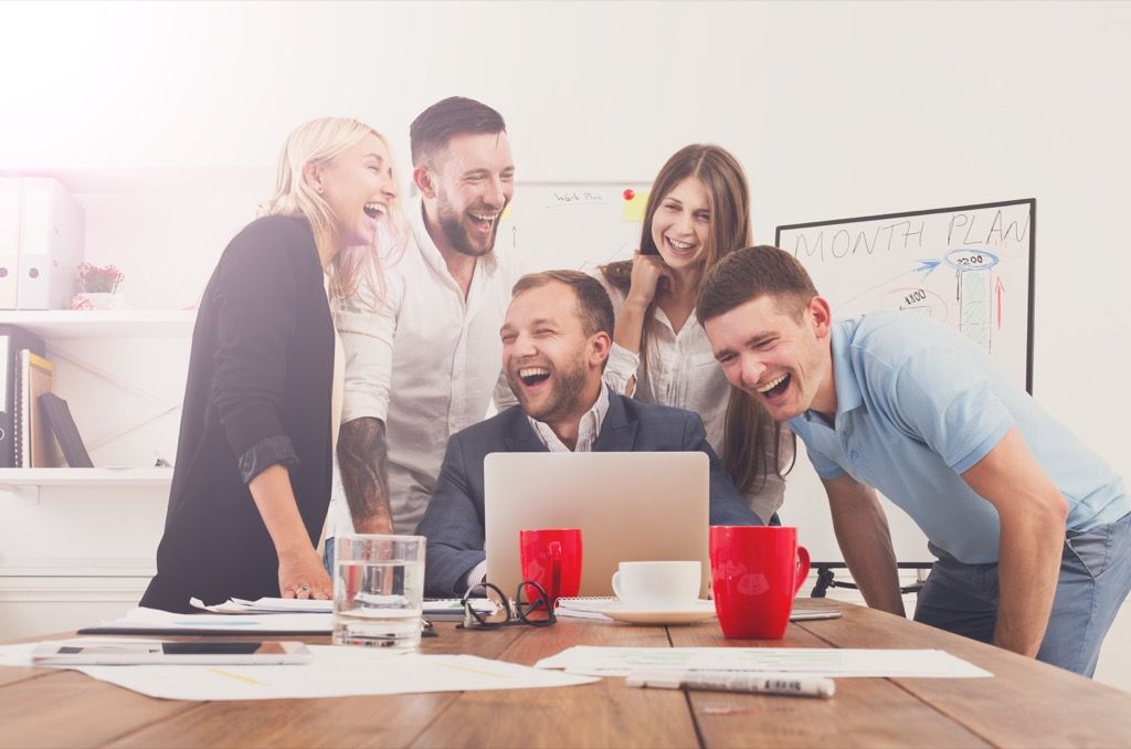 kollegor samlade runt en bärbar dator skrattar Signs Your Boss Wants to Fire You