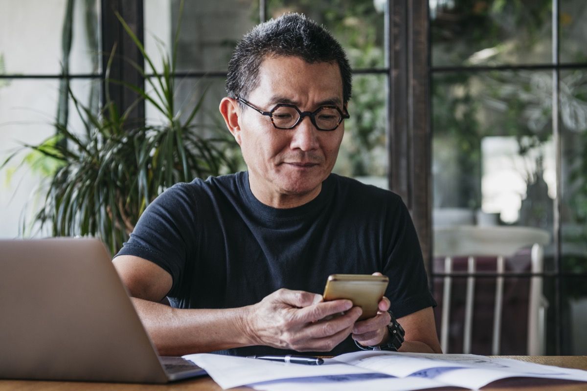 Азиатски мъж на около 50 години работи дистанционно, използва мобилен телефон, комуникация, връзки, технологии
