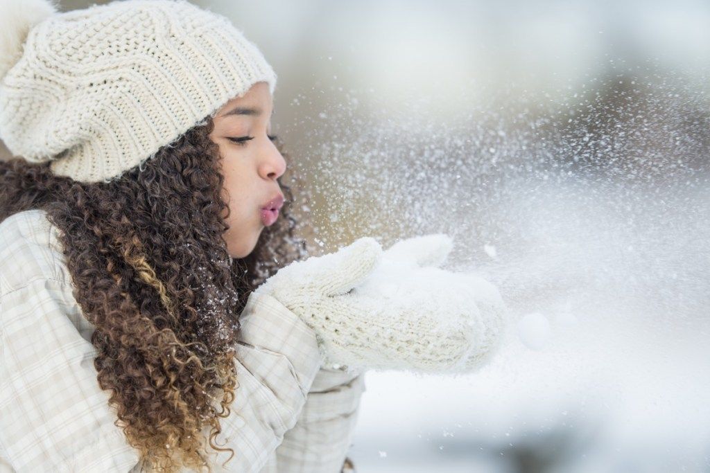 deklica, ki piha sneg z rokavicami