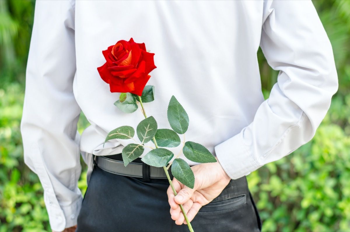Žmogus, už nugaros laikantis raudoną rožę