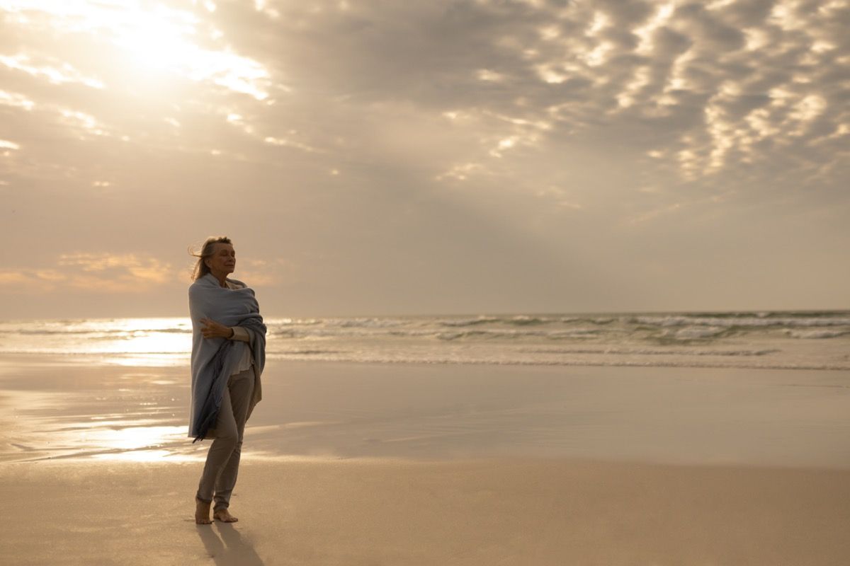 Vanhempi nainen seisoo yksin rannalla