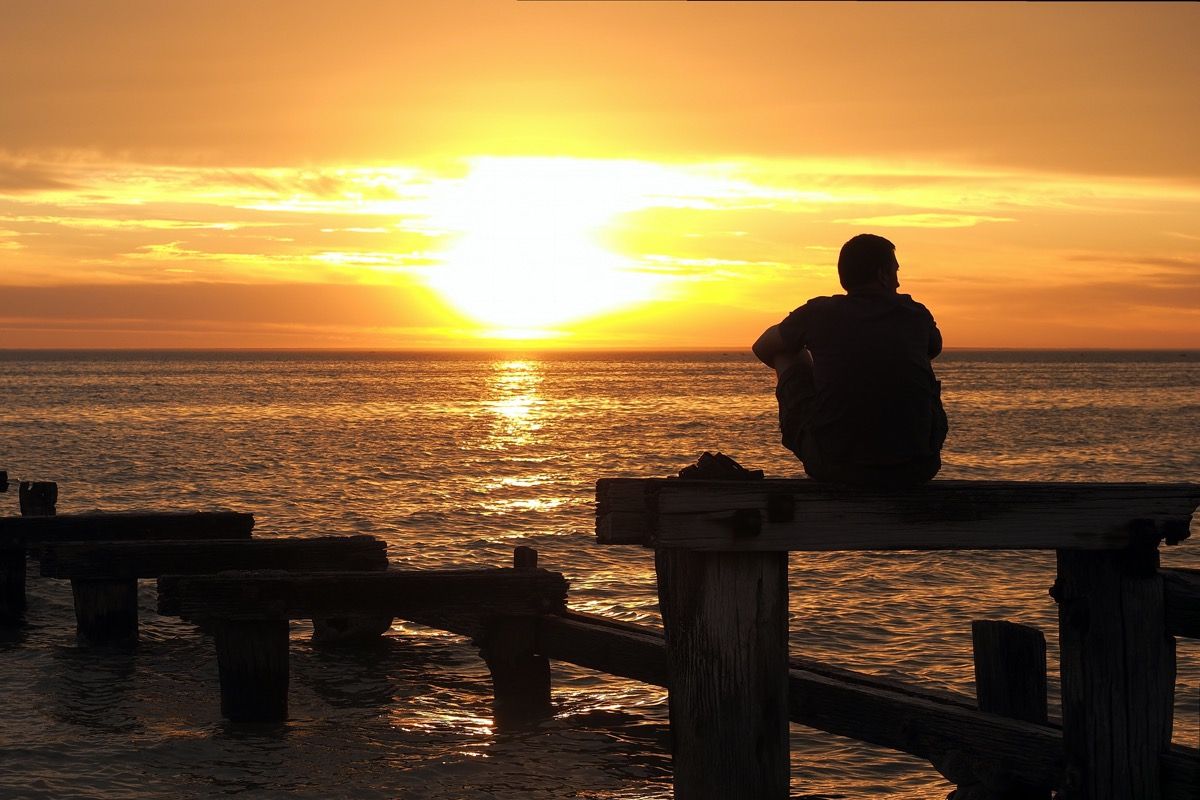 Mies istuu telakalla auringonlaskun aikaan katsellen vettä