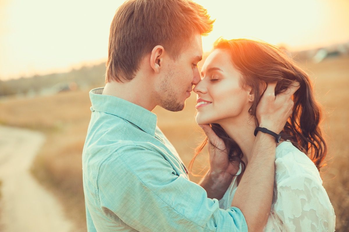 Moški in ženska, ki se bosta poljubila na polju ob sončnem zahodu