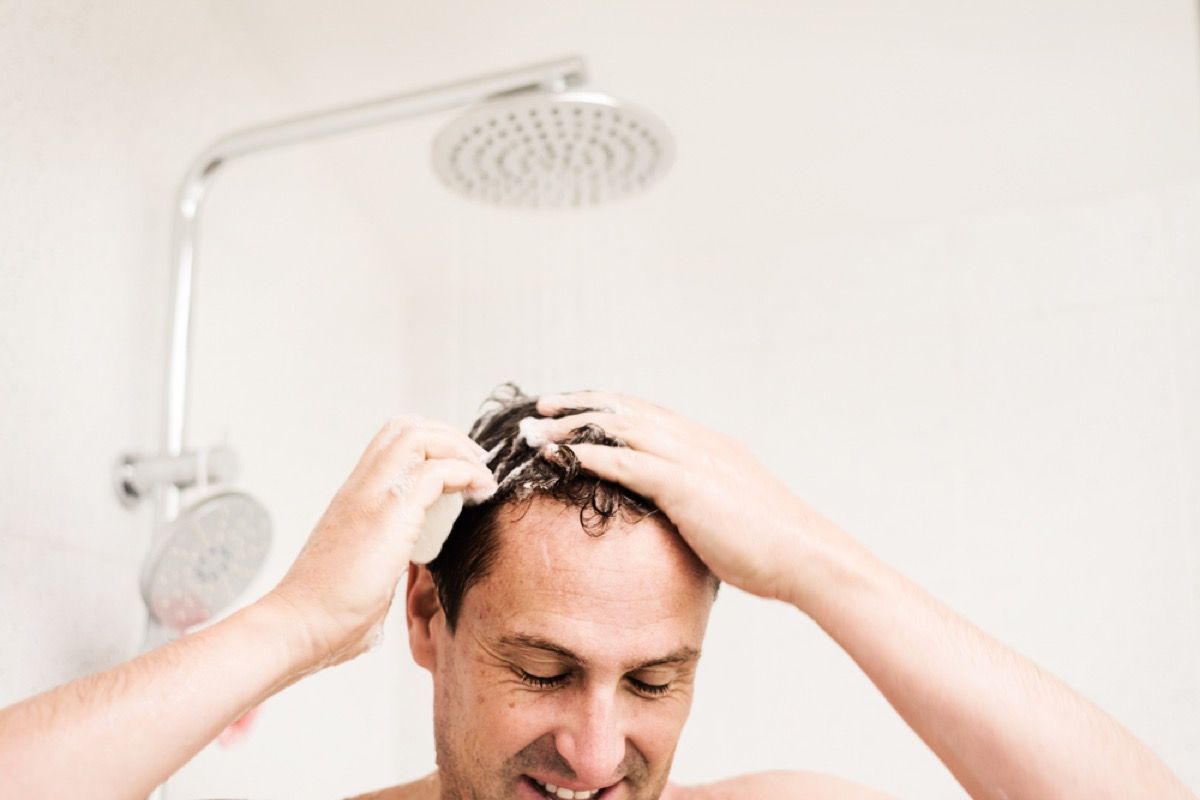 keski-ikäinen mies saippuaa hiukset suihkussa