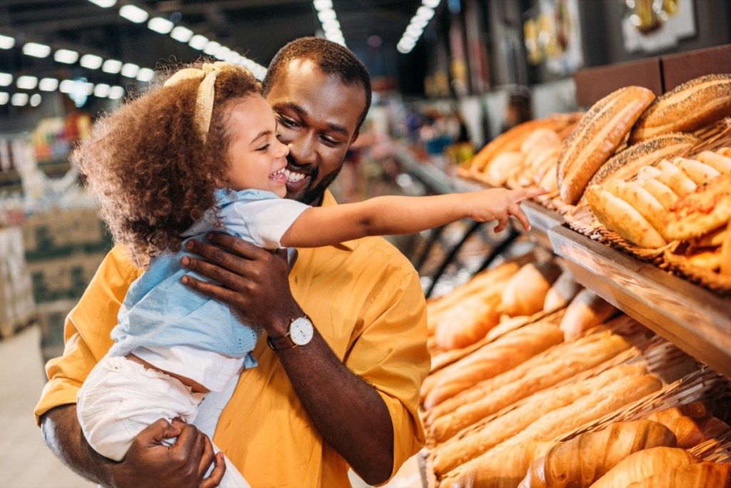 tētis un meita pārtikas veikalā skatās uz maizi