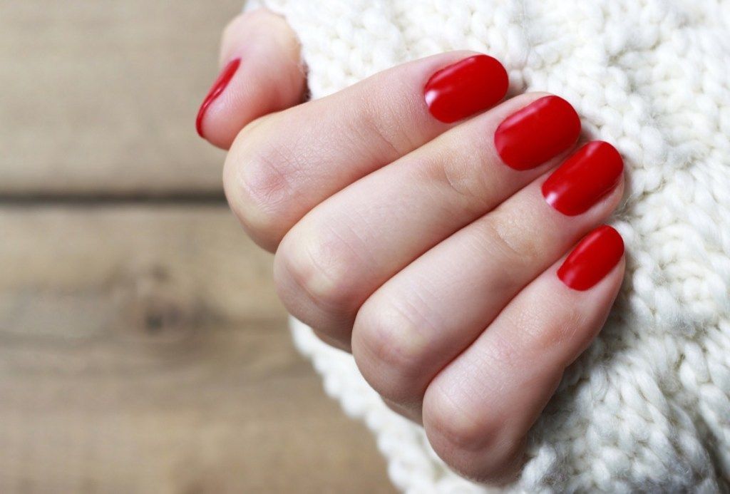 Tangan wanita dengan manikur merah di latar belakang rajutan putih dengan ruang salinan, pandangan atas