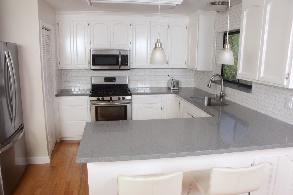 модерна кухня със сиви каменни плотове и бели шкафове и подплата на плочките на метрото