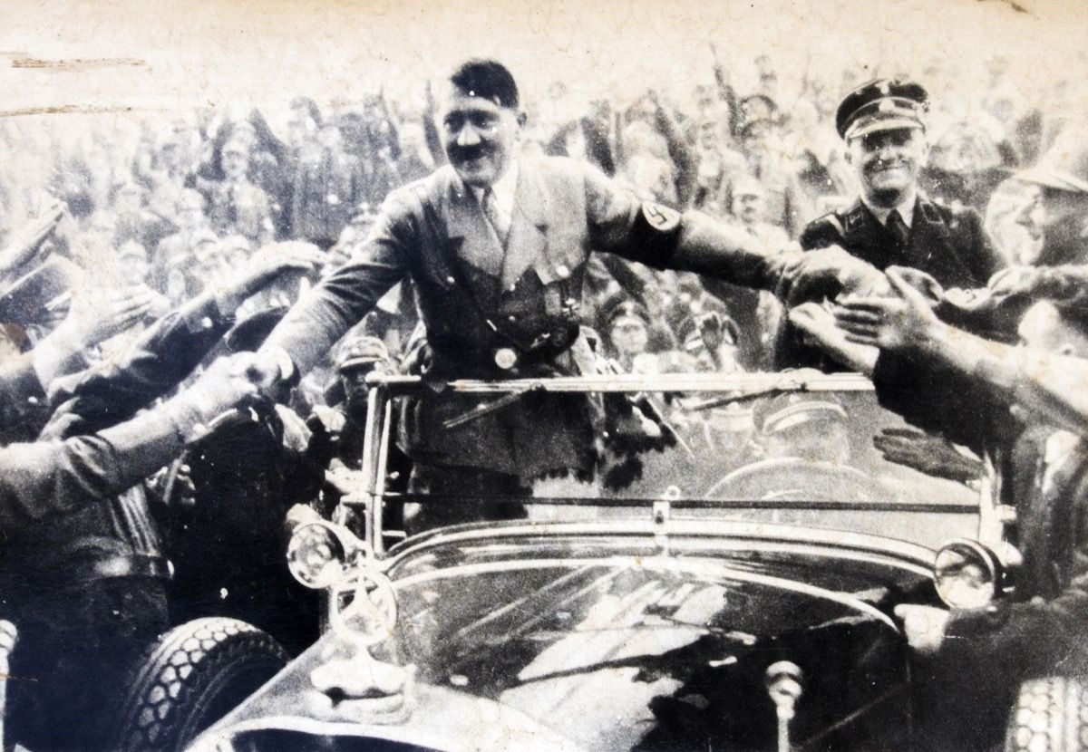 जर्मनी - CIRCA 1940s: एडॉल्फ हिटलर अपने प्रशंसकों के साथ एक परिवर्तनीय और मिलाते हुए हाथ में खड़ा है, एंटीक फोटो का प्रजनन