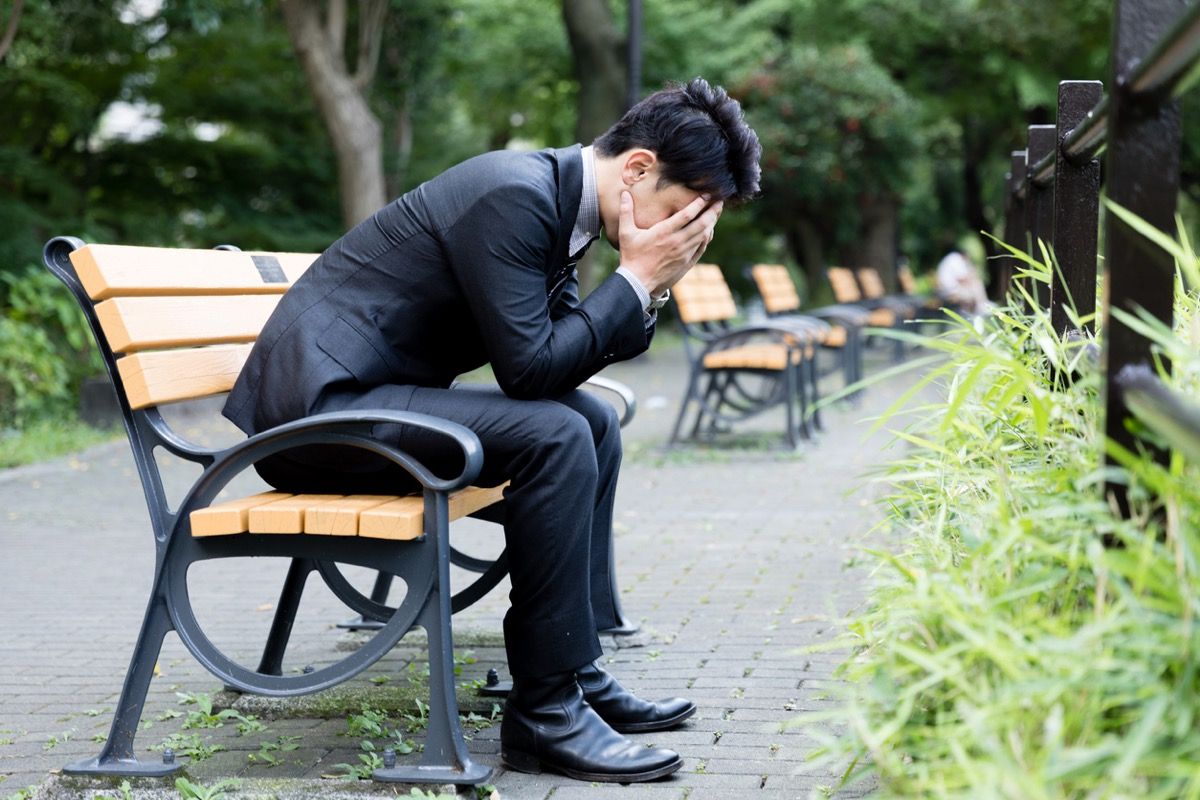 азиатски мъж в костюм, седнал на пейка с глава в ръце