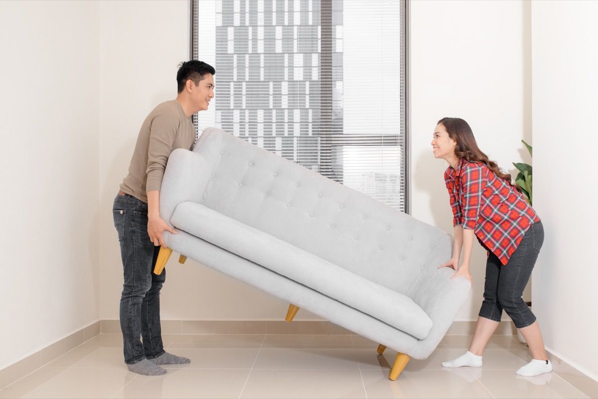 Paar, das Möbel in ihrem Wohnzimmer neu anordnet und eine Couch zusammen bewegt