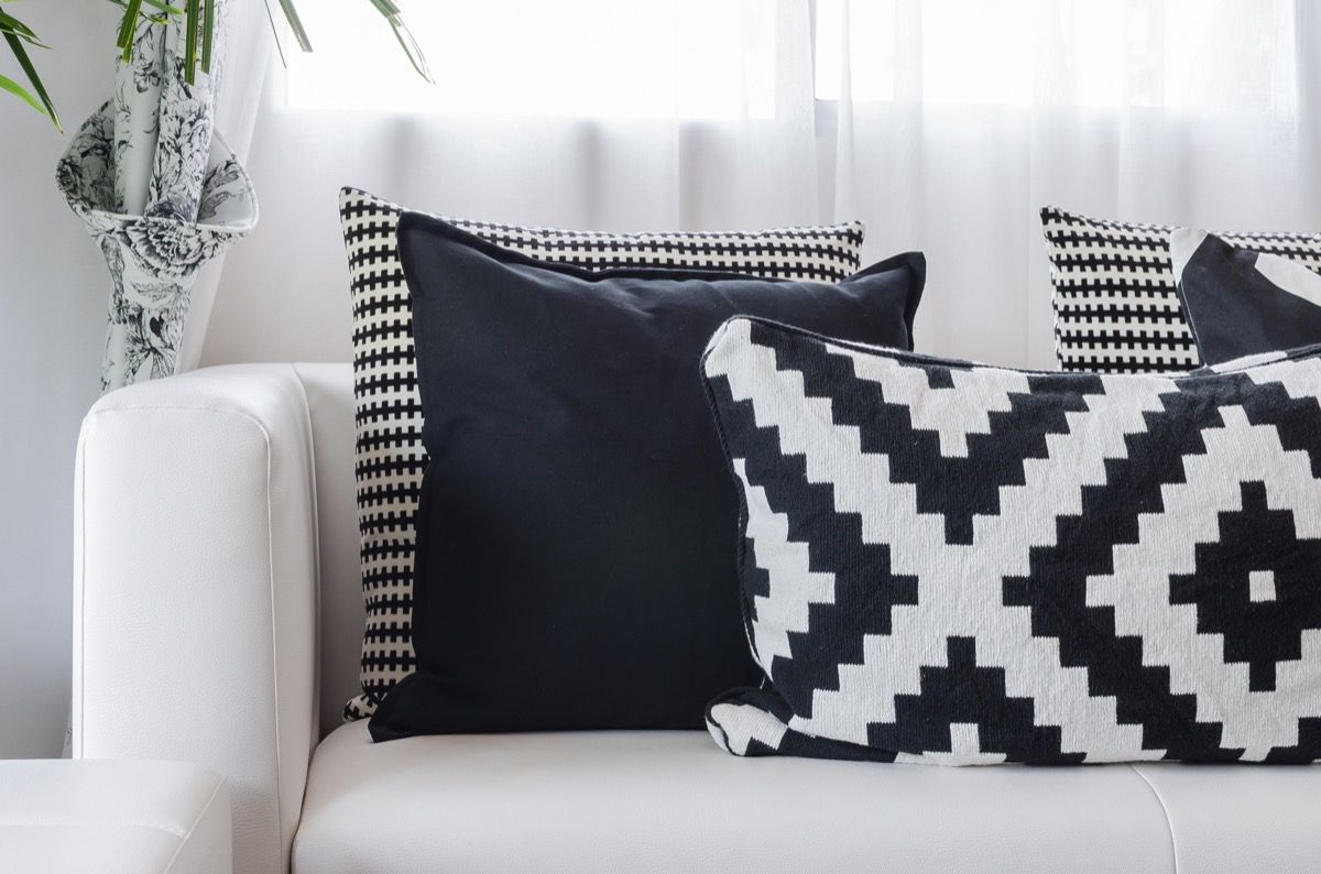 Kelios skirtingos juodai baltos raštuotos pagalvės, atsiremiančios į baltą sofą