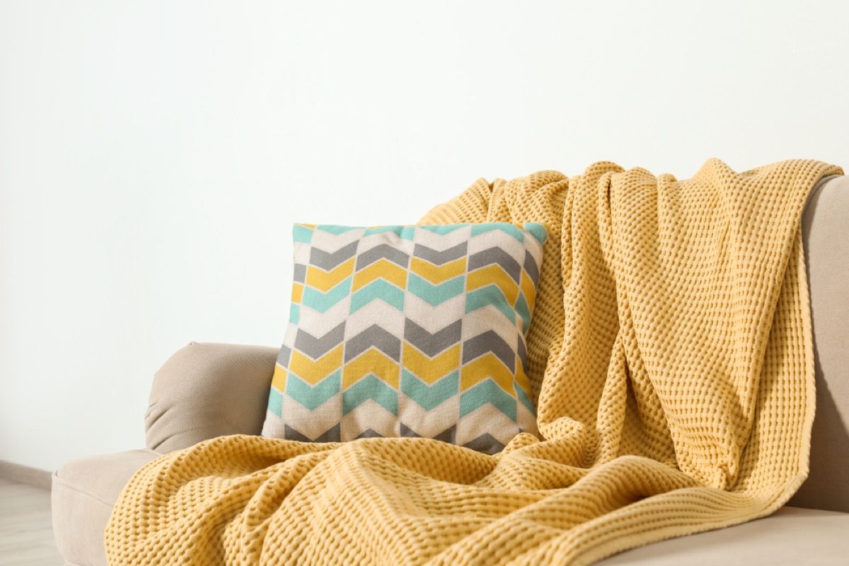 gult kasteteppe og mønstret pute på en sofa
