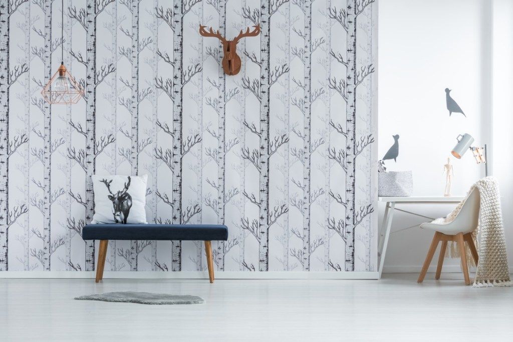 modernong silid-tulugan na may puting puno ng wallpaper at faux deer head at itim na upholstered bench