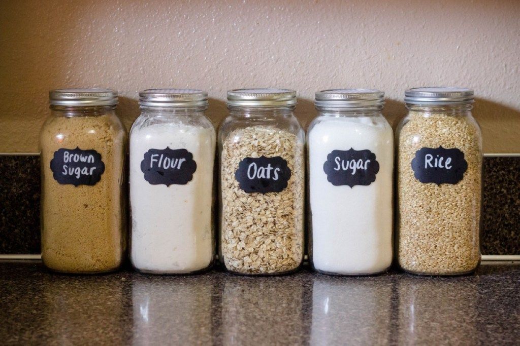 stikliniai indeliai su miltais, cukrumi, avižomis ir ryžiais ant virtuvės stalviršio