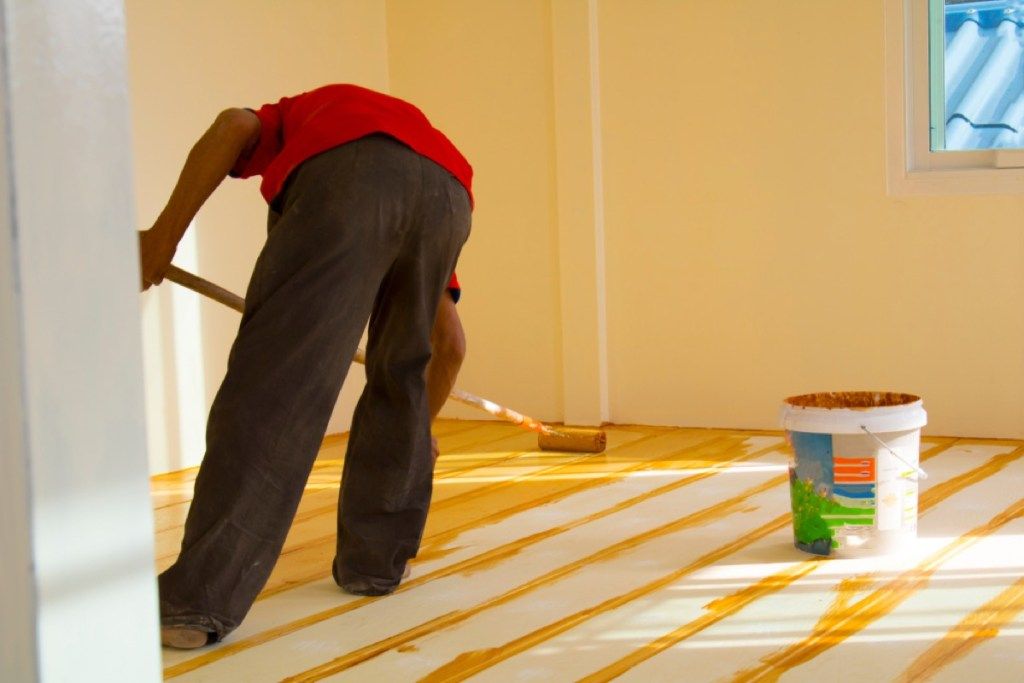 homem de camisa vermelha e calça preta pintando o piso de madeira de amarelo